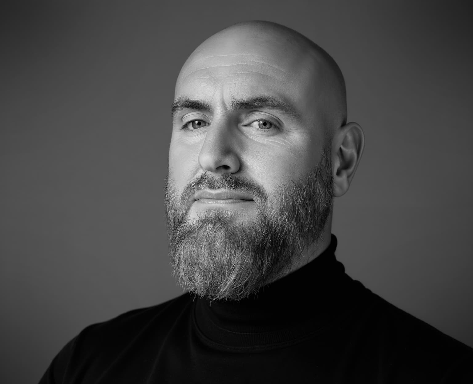 Black and white portrait of a bald man with a beard in a black turtleneck.